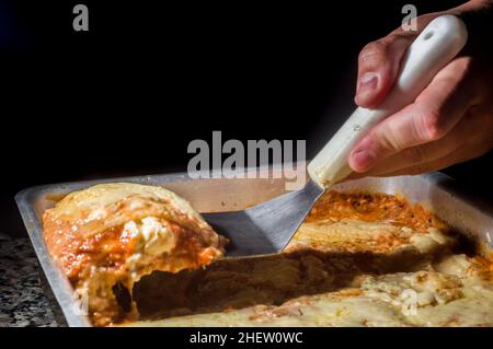 lasagna in an aluminum pan, spatula taking a piece of the pan, selective  focus Stock Photo - Alamy