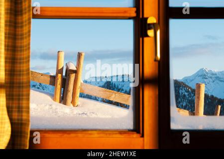 view through window of a hut with very much snow and mountains at a winter day Stock Photo