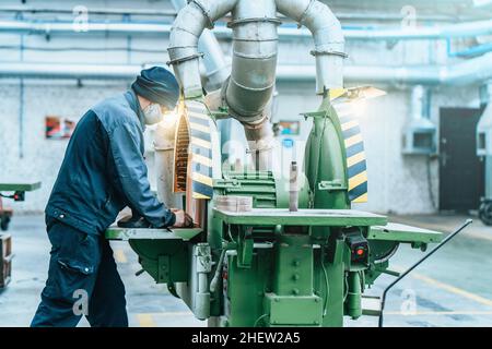 Worker in uniform work at big industrial grinder machine in wood factory for furniture production. Stock Photo