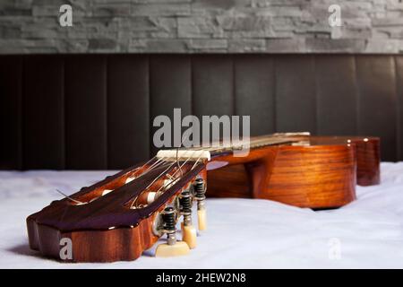 classical guitar lying on the bed in front of a brown leather back and a stone wall Stock Photo