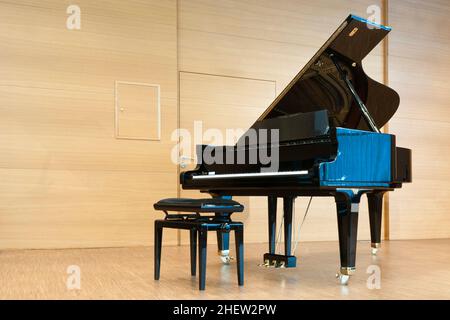 opened black grand piano with stool on a wooden concert stage Stock Photo