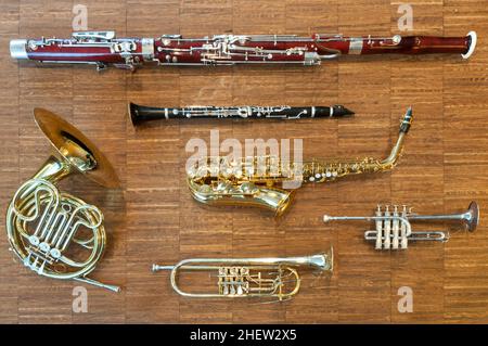 several wind instruments laying on a wooden floor. trumpet, horn, saxophone, clarinet, flute,  bassoon, curtal