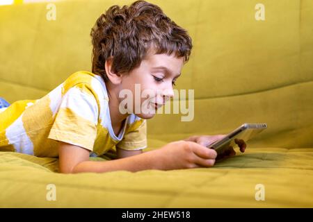 boy in yellow and white t-shirt enthusiastically plays a game on a tablet Stock Photo
