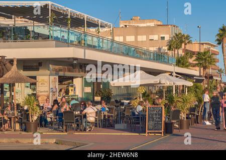 People friends relax sitting under the umbrella on the terrace in a bar on the promenade of Santa Pola, Spain, Europa Stock Photo