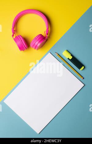 pink wireless headphones, fluorescent, pencil and a sheet of paper placed on a diagonally divided background, top view Stock Photo