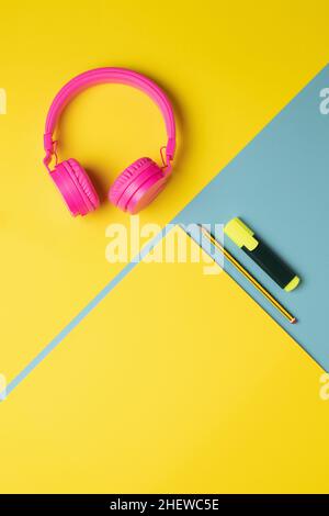Fluorescent marker and pencil aligned with a yellow cardboard and pink headsets on a two-color vertical background Stock Photo