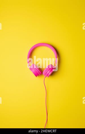 pink wired headphones centered on a flat yellow background, vertical image Stock Photo