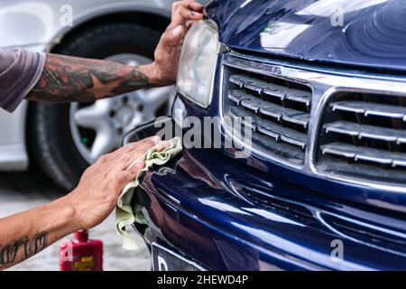 Tattooed man hand polish and rub a blue car bumper with cloth to get clean , shine and detail surface on the garage. Suitable for paint work and detai Stock Photo