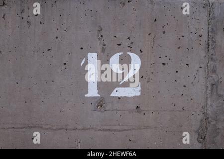number 12 printed on a concrete wall full of small holes Stock Photo
