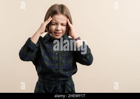 Child has a headache. Kid Little Girl 9s Wearing Plaid Shirt Dress feeling sick and stressed. Health problem. Healthcare And Medicine Concept. Free space for text. Stock Photo