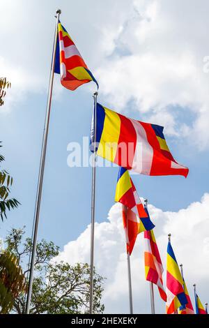 Buddhist flags waving in wind under blue cloudy sky at the entrance of a temple in Sri Lanka. The Buddhist flag is a flag designed in the late 19th ce Stock Photo