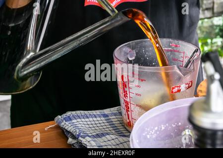 metallic chrome traditional vintage water jug or teapot pouring the brown tea into the measuring cup Stock Photo