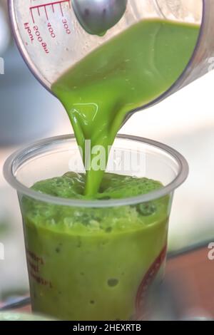 pouring a fresh and creamy milk green tea in measuring cup into a transparent plastic glass with cold shaved ice inside with blurry and soft focus bac Stock Photo