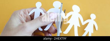 Woman hand cuts paper figures in form of family with scissors closeup Stock Photo