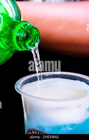 Pouring a soda water into a transparent plastic glass with cold shaved ice inside and and fresh sour limes sliced on top for a mojito drink for with a Stock Photo