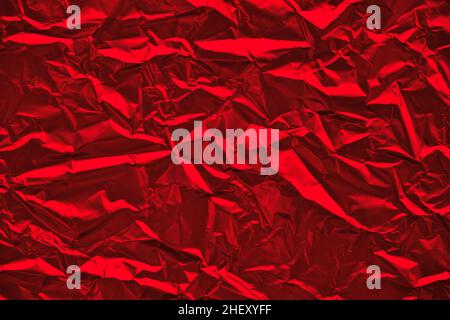 Close-up of crumpled silver aluminum foil texture in red tone. Abstract background for design. Stock Photo