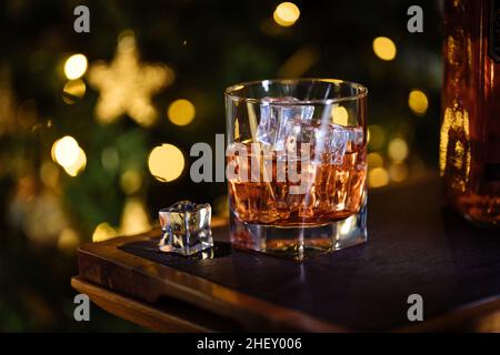 Glass of Whiskey or aperol spritz with ice cubes in a festive Christmas mood with Christmas tree in background Stock Photo