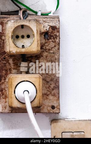 rough and dull old electric socket hanging on the white wall Stock Photo