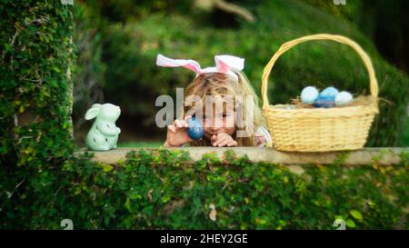 Child with rabbit ears, Easter holidays. Kid hunting Easter eggs in easters basket. Cute bunny boy, funny kids portrait. Stock Photo