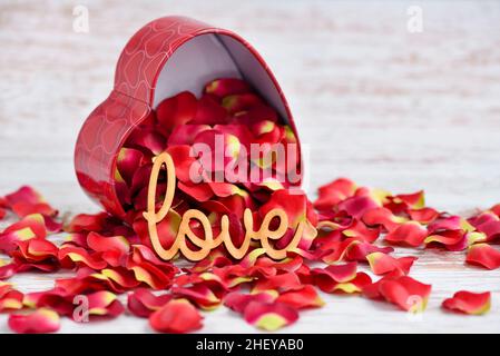 The word "Love" on a background of red rose petals falling out of a heart-shaped box Stock Photo