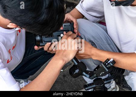 a young man photographers working as a team to setting up the camera and gimbal for their job on the sidewalk Stock Photo