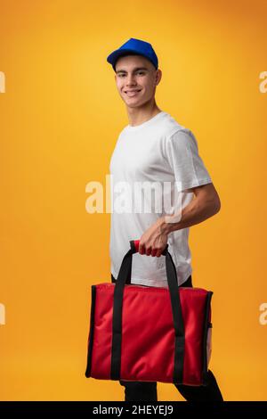 Portrait of pizza delivery boy with thermal bag against yellow background Stock Photo