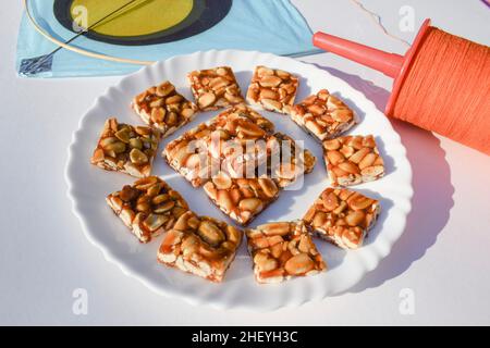 Peanut chikki or Moongfalli chikky bars with Kite and spool string with white background. Makar sankranti, uttarayan, pongal, Lohri festival posters f Stock Photo