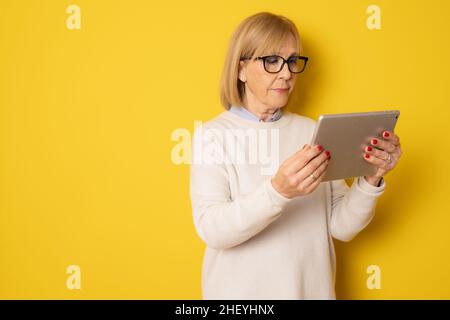 Senior woman using tablet isolated on yellow background Stock Photo