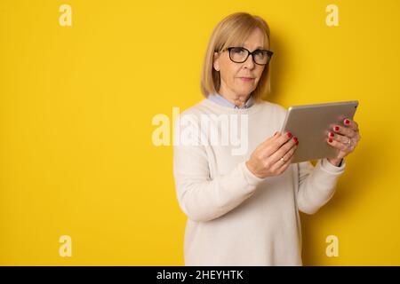 Senior woman using tablet isolated on yellow background Stock Photo