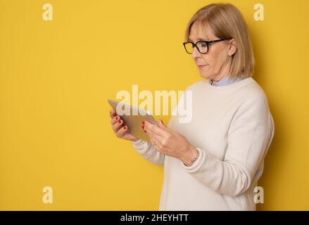 Senior woman using tablet isolated on yellow background Stock Photo