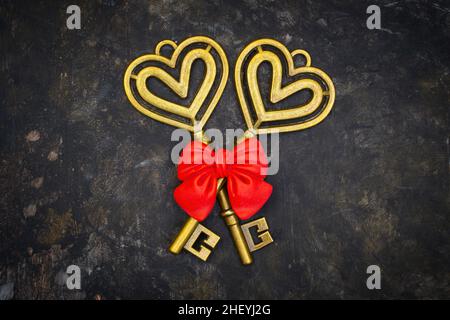 Crossed antique style skeleton keys with a red bow on a dark grungy table. Symbolic romantic concept. Stock Photo
