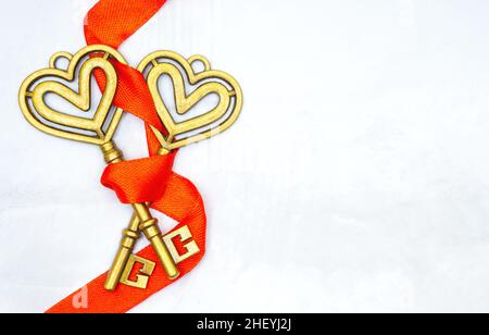Close-up of two vintage keys wrapped together with a red ribbon on a neutral background with copy space. Strong marriage creative concept. Stock Photo