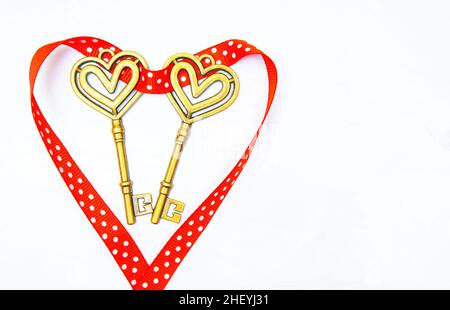 Two gold-toned skeleton keys wrapped with a dotted red ribbon laid out in the shape of a heart on a neutral background. Stock Photo
