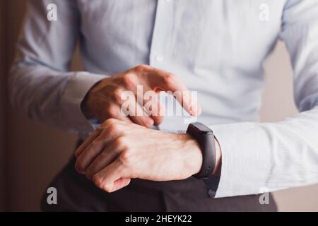 Office man in blue shirt, using smart watch or bracelet. Touching screen to set Technology lifestyle Stock Photo