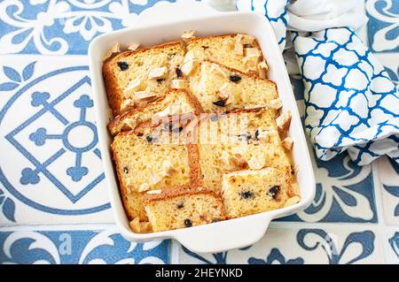 Bread (panettone) pudding from leftovers with custard and raisins in a baking dish on a blue background. Top view. Stock Photo