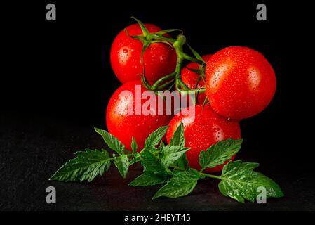 Ripe organic tomatoes on the black table in low key with water drops Stock Photo