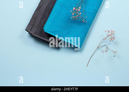 Stack of soft terry towels with decorative branches on the blue background. Spa products. Top view. Stock Photo