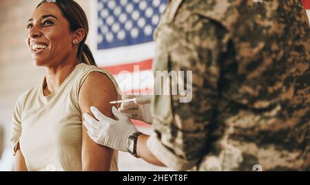 Servicewoman receiving a dose of the covid-19 vaccine in her arm. American soldier smiling happily while getting inoculated against coronavirus diseas Stock Photo