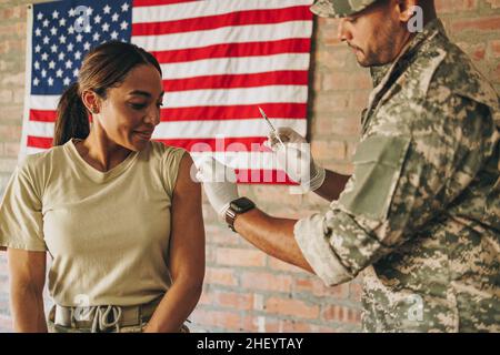 Cheerful female soldier getting inoculated against the flu in the military hospital. United States servicewoman receiving a dose of the influenza vacc Stock Photo