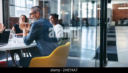 Cheerful mature businessman attending a meeting with his colleagues in an office. Experienced businessman smiling while sitting with his team in a mee Stock Photo