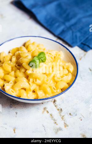 Classic mac and cheese with basil on top and mac and cheese baked in oven in background with forks and raw macaroni on a rusticžwooden background Stock Photo