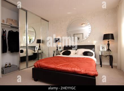 Bedroom in modern showhome, double kingsize bed, orange quilt quilted bedspread duvet cover,bedside lights,feature wall wallpaper,mirrored wardrobes Stock Photo
