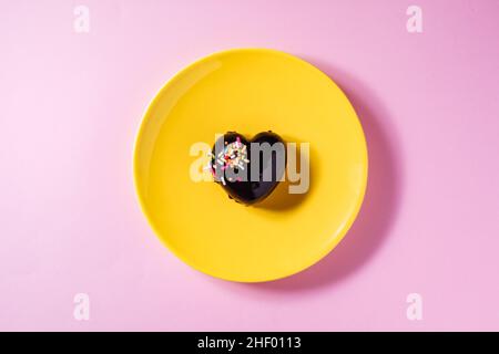 Heart shaped chocolate cake on a yellow plate with heart shaped chocolate pralines on a purple background with two red ribbons. Valentine day Stock Photo