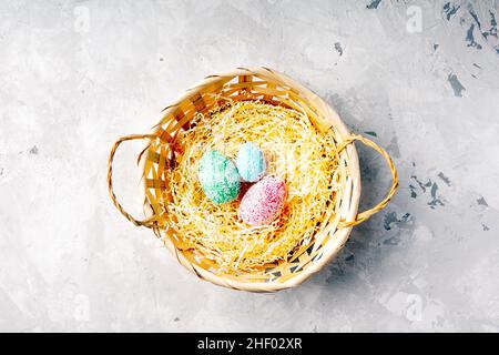 Pink green blue pastel eggs in basket on grey background with space for text. Happy easter. Stock Photo