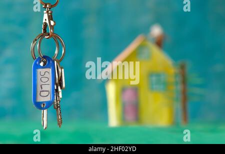 latchkey with key fob and sold marking, blurred model home in the back,buying house,real estate concept.Selective focus,free copy space Stock Photo