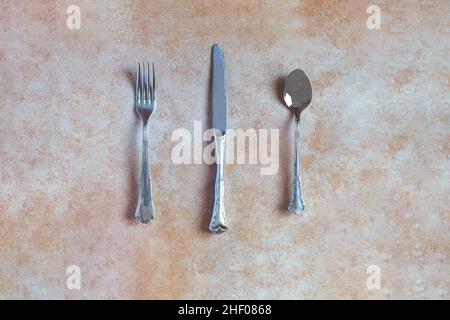 Overhead view of an antique silver cutlery consisting of a fork, spoon, and knife on an abstract background and ceramic texture with pastel color. Ant Stock Photo
