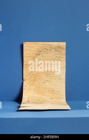 A weathered and old wood texture like parchment on a colorful textured blue-painted pedestal platform background. Art and writing. Stock Photo