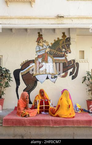 Three Indian female musicians entertain tourists in front of a mural of a horse in the Udaipur City Palace Complex, Udaipur, Rajasthan, India Stock Photo