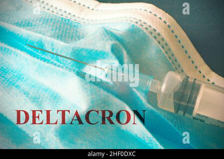 Top view of a syringe laying on surgical mask with the text 'Deltacron' new Covid-19 variant. Stock Photo