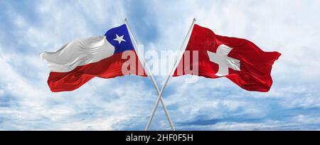 two crossed flags Chile and Switzerland waving in wind at cloudy sky ...
